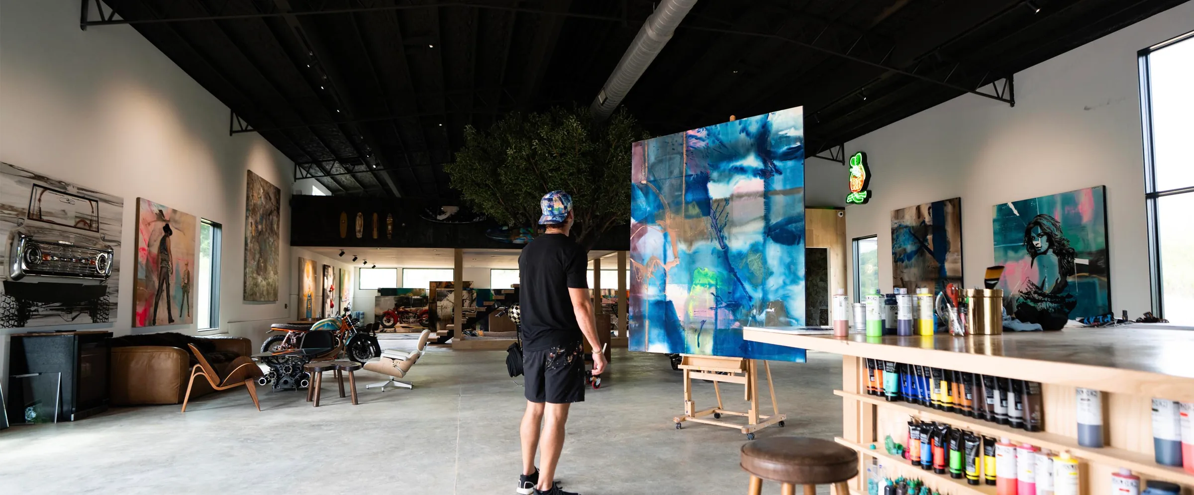 Erik Skoldberg walking through his Kingston Springs studio barn — a large blue Urban Collection canvas on the far wall, racked spray cans along the counter, motorcycles and the olive tree beyond