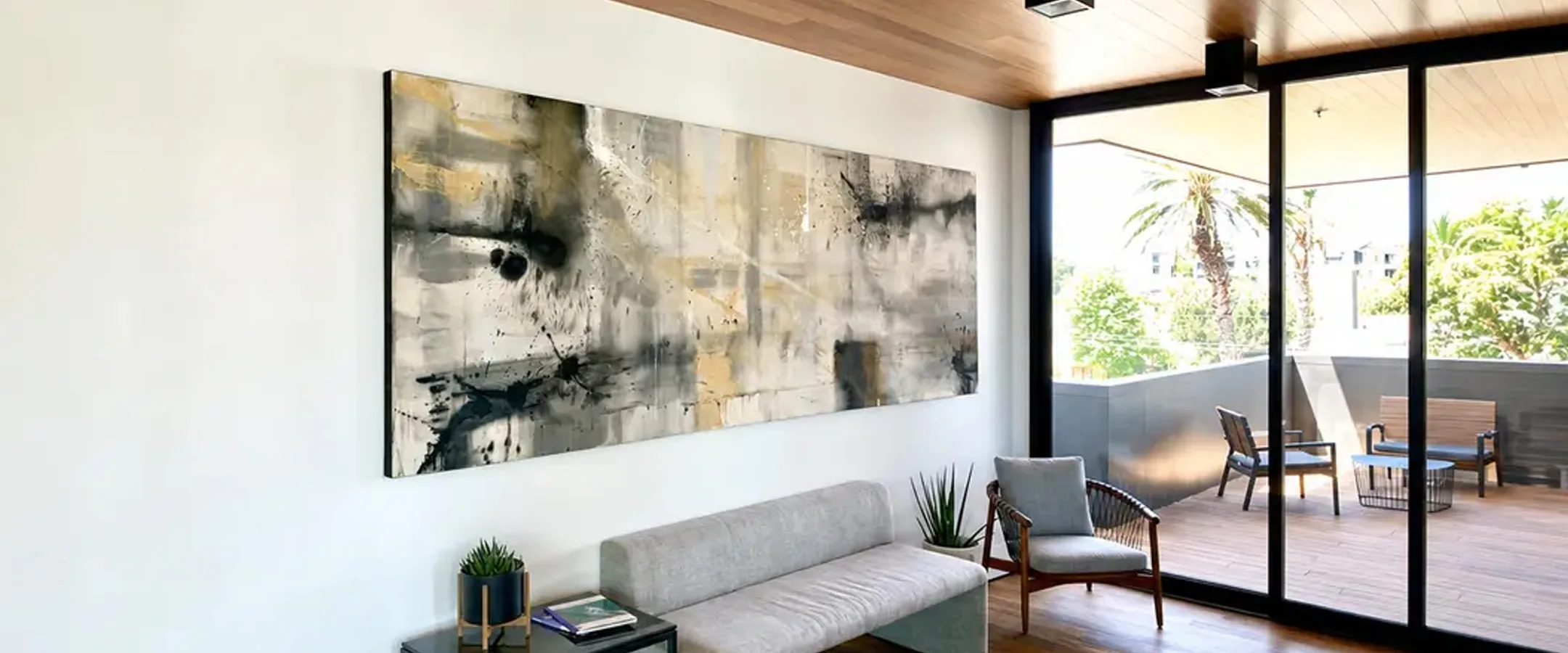 A long horizontal Urban Collection painting by Erik Skoldberg in black, ochre and cream on a white wall beside a glazed terrace
